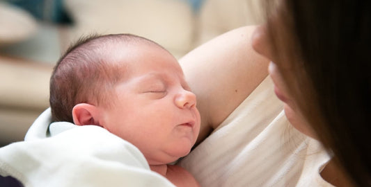 Madre primeriza sostiene en brazos a su recién nacido dormido, en un ambiente cálido y tranquilo