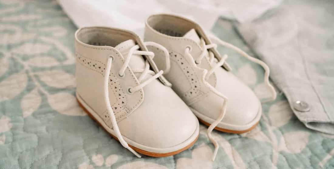 Zapatos blancos de bebé con cordones, colocados sobre colcha en tonos suaves, ideales para looks en días especiales