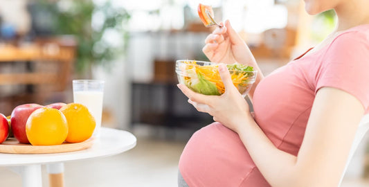 Mujer embarazada comiendo una ensalada saludable con frutas y un vaso de leche, alimentación equilibrada durante el embarazo.